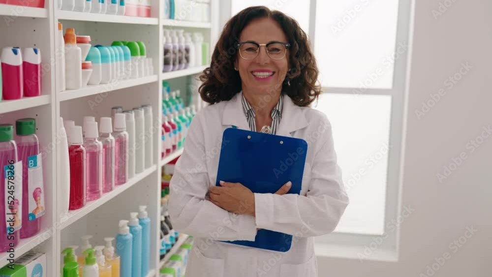 Sticker Middle age woman pharmacist smiling confident holding clipboard at pharmacy