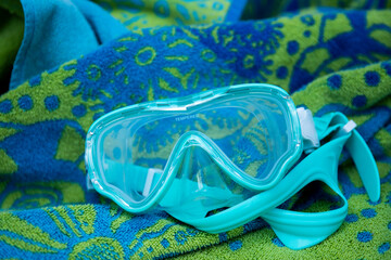 blue swimming googles resting on blue and green beach towel, near the pool