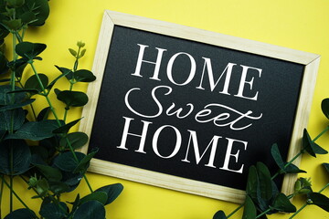 Home Sweet Home typography text written on wooden blackboard with green eucalyptus decoration on yellow background