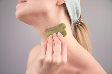 Close-up portrait of a young woman massaging her neck with a gouache scraper. 