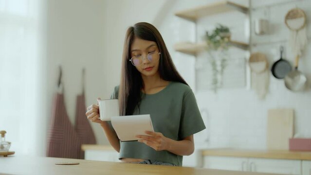 Happy young asian woman wearing glasses in kitchen at home. Female concentrate reading note cooking