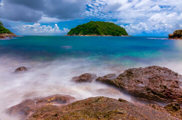 Naiharn Beach in Phuket Thailand, turquoise blue waters, lush green mountains colourful skies. Phuket is a tropical island many palms