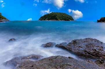 Naiharn Beach in Phuket Thailand, turquoise blue waters, lush green mountains colourful skies. Phuket is a tropical island many palms