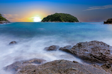 Naiharn Beach in Phuket Thailand, turquoise blue waters, lush green mountains colourful skies. Phuket is a tropical island many palms