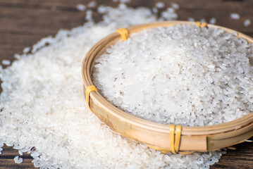 Wooden spoon full of rice in bamboo basket full of rice grains on table