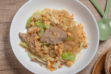 Stir fried vermicelli with pork, egg and collard greens in a white plate.