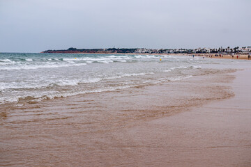Fototapeta premium people walking along the seashore, early in the morning, at La Barrosa beach in Sancti Petri, Cadiz, Spain