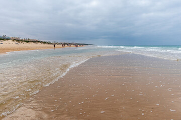 people walking along the seashore, early in the morning, at La Barrosa beach in Sancti Petri, Cadiz, Spain