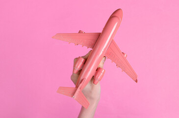 Hand holding pink air plane on pink background. Minimalism travel concept