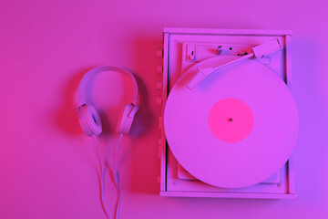 White vinyl record player with headphones in pink-blue neon gradient light. Minimalism music concept. Top view