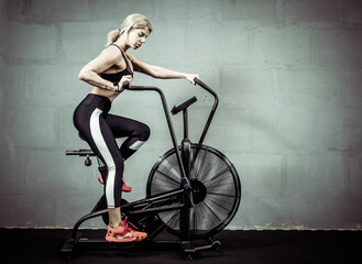 Obraz na płótnie Canvas Woman doing intense cardio training on exercise bike. Fitness female using air bike for cardio workout at gym