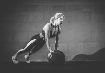 Sportswoman doing push ups exercise with medicine ball. Muscular woman exercising fitness ball at gym