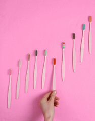Hand selects Eco-friendly bamboo toothbrush among the set on pink background