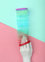 White hand and Rainbow plastic multicolored spiral slinky toy on pink  blue background. Minimalism