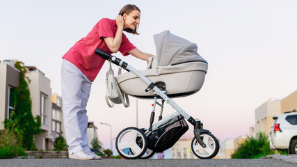 A young mother walks with her child around the city in a stroller. A woman in a pink T-shirt walks with her newborn baby in the city