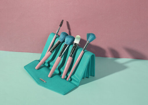 Beauty and fashion minimalistic scene. Makeup brushes and purse on blue pink pastel background with trendy shadows. Creative layout