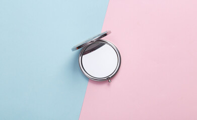 Women's portable make-up mirror on a blue-pink pastel background. Top view