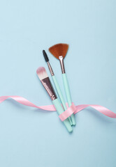 Set of make-up brushes wrapped with a pink ribbon on a blue background