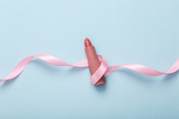 Obraz na płótnie Canvas Pink lipstick with pink ribbon on blue background