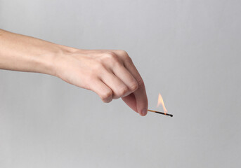 Hand holds a dying match on a gray background