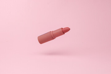 Red lipstick tube flying in antigravity on pink background with shadow. Levitation object in the...