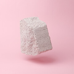 Porous block stone flying in antigravity on pink background with shadow. Levitation object in the air. Creative minimal layout
