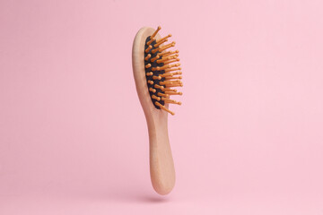 Eco wooden hair brush flying in antigravity on pink background with shadow. Levitation object in...