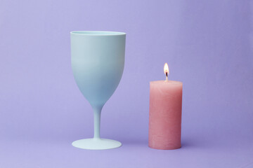 A plastic wine glass with a flaming candle on a purple background. Pastel color trend