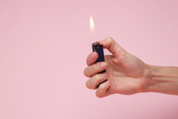 Hand holding a lighter with a flame on a pink background - obrazy, fototapety, plakaty