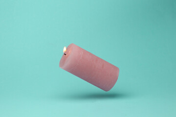 Pink flaming candle flying in antigravity on mint green background with shadow. Pastel color trend. Levitation object in the air. Creative minimal layout