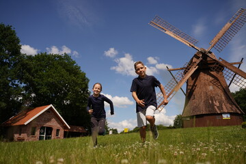 Children cheerfully run on the grass against the background of the sky and mill