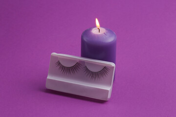 Purple burning candle and false eyelashes on purple background. Spa salon