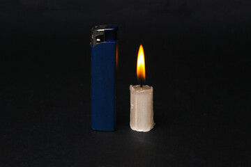 Lighter with flaming candle on black background