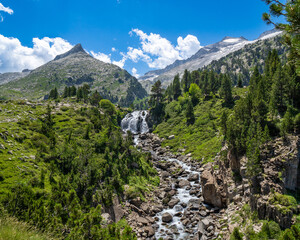 Fototapeta na wymiar Spectacular river with large stones coming down from a waterfall in the Aragonese Pyrenees of Benasque. Mountains and clouds in the background.