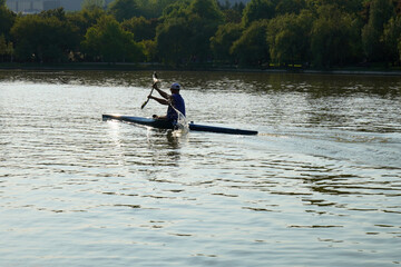 Fit active man paddling in a kayak on lake water in Titan park in Bucharest on summer day, making sparkling water splash. Contre-jour image