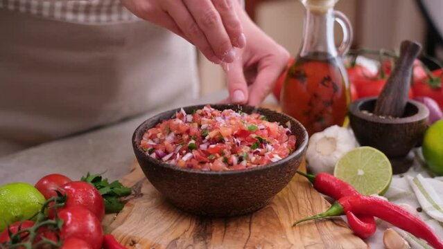 woman salting salsa dip sauce in wooden bowl at domestic kitchen