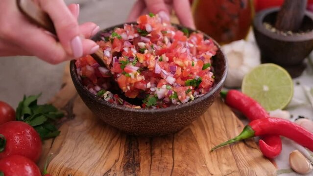 Slow motion shot of woman mixing salsa dip sauce ingredients in wooden bowl