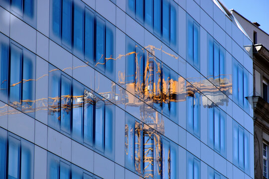 glass office building elevation detail with blue sky. yellow steel tower crane reflecting in the windows. modern architecture concept. abstract view. summer scene. metal truss crane truss and boom