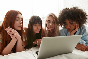 Fototapeta na wymiar Young multiethnic girlfriends watch laptop on bed