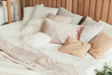 Lots of pillows in soft colors on a bed in a room with a neutral aesthetic