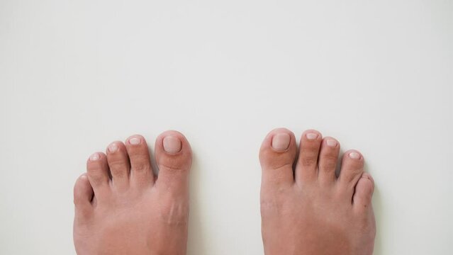 First person top view 4k stock video footage of two female pedicured feet isolated on white empty background. Pov or fpv footage of professional pedicure treatment of female legs, toenails painted