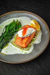 Grilled salmon fillet with zucchini, spinach, cream cheese, garnished with red caviar with cream sauce in a ceramic plate on a dark textured background. Restaurant menu Isolated on black