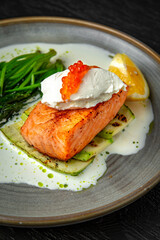 Grilled salmon fillet with zucchini, spinach, cream cheese, garnished with red caviar with cream sauce in a ceramic plate on a dark textured background. Restaurant menu Isolated on black