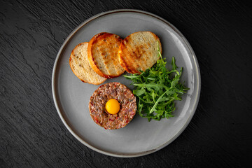 Beef tartar with spices and quail egg in a ceramic plate on a dark textured background. Restaurant menu Isolated on black