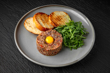 Beef tartar with spices and quail egg in a ceramic plate on a dark textured background. Restaurant menu Isolated on black