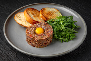 Beef tartar with spices and quail egg in a ceramic plate on a dark textured background. Restaurant menu Isolated on black