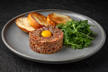 Beef tartar with spices and quail egg in a ceramic plate on a dark textured background. Restaurant menu Isolated on black