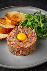 Beef tartar with spices and quail egg in a ceramic plate on a dark textured background. Restaurant menu Isolated on black
