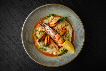 Delicate risotto with champagne and seafood: langoustines, mussels, squids in a ceramic plate on a dark textured background. Restaurant menu Isolated on black