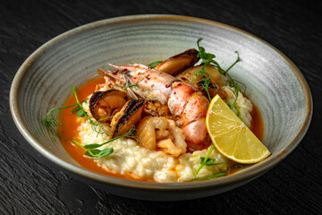 Delicate risotto with champagne and seafood: langoustines, mussels, squids in a ceramic plate on a dark textured background. Restaurant menu Isolated on black